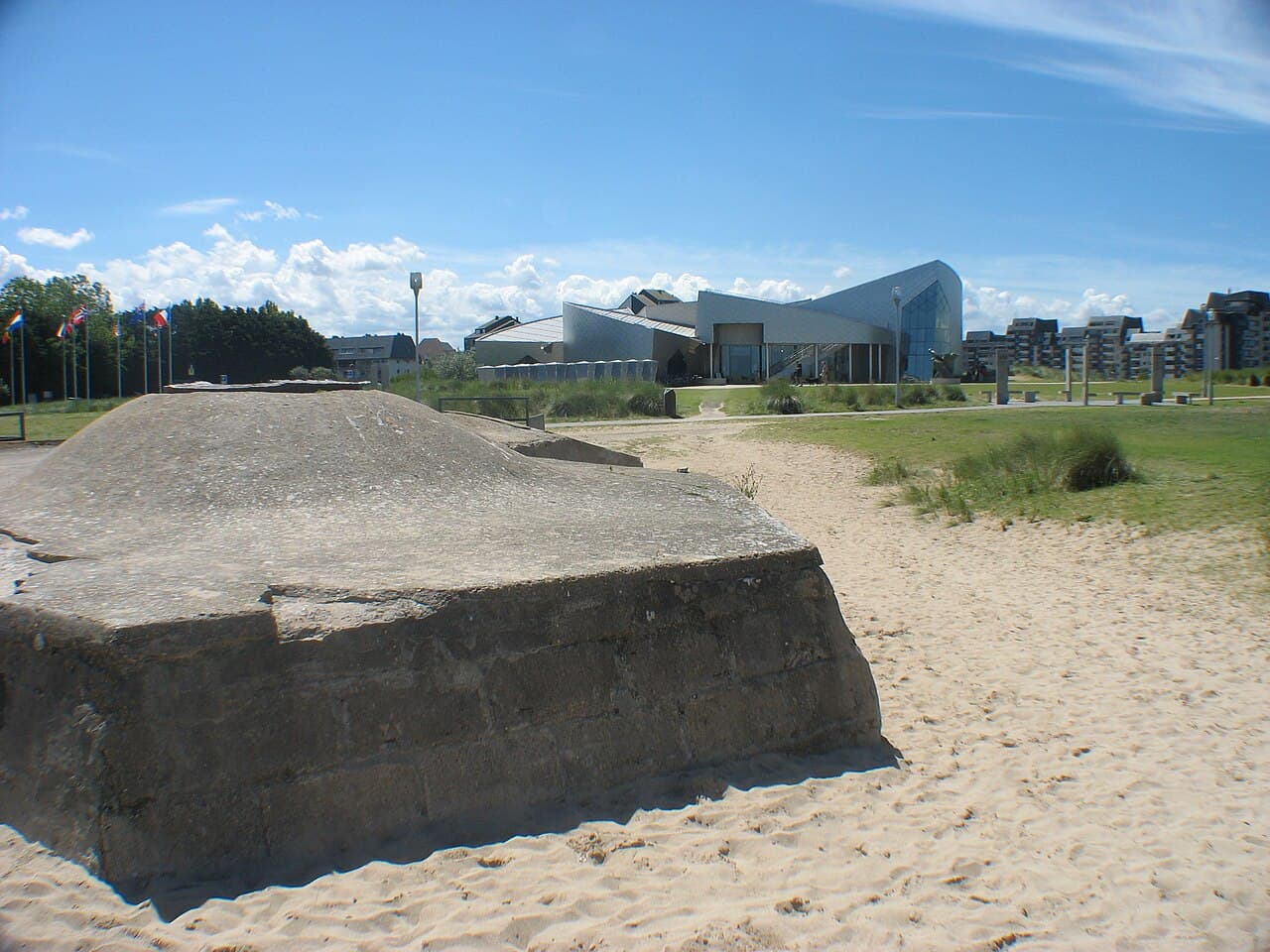 A WWII German bunker on the sand with the modern Juno Beach Centre building behind it, Courseulles-sur-Mer